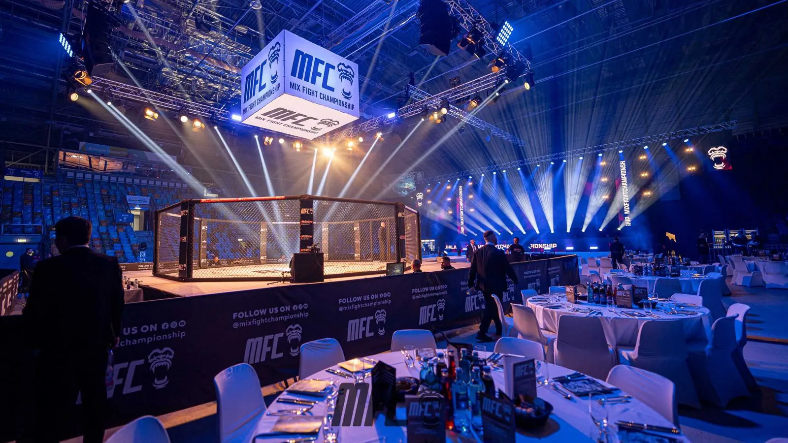Gala der Mix Fight Championship: festlich gedeckte VIP-Tische vor dem beleuchteten Käfig, darüber ein großer Würfel mit MFC-Logo, an der Bande MFC-Schriftzüge